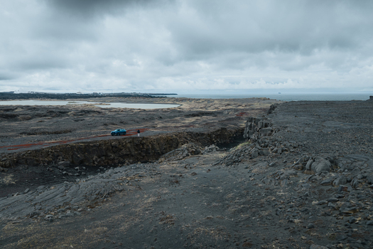 Aerial view of the volcanic landscape at Sandfellshaed Viewpoint featuring rugged lava fields a car on a road and the distant coastline in Keflavik Reykjanesbaer Iceland.