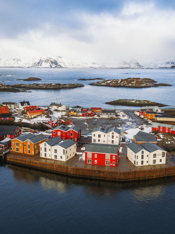 Aerial view of red and white buildings nestled on the edge of the harbor reflecting in the dark water Henningsv&aelig;r Nordland Norway.