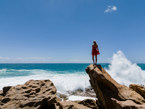 Aerial view of a woman in a red dress standing on a rock formation at Injidup Natural Spa with crashing waves and blue ocean in Yallingup Western Australia Australia. Aerial view of a woman in a red dress standing on a rock formation at Injidup Natural Spa with crashing waves and blue ocean in Yallingup Western Australia Australia.