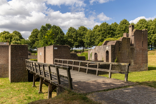 View of a historic wooden footbridge leading to ancient brick fortifications surrounded by green grass and trees in Heusden North Brabant Netherlands.