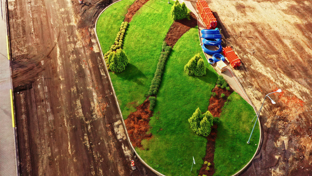 Aerial view of a landscaped green island surrounded by construction work with blue and orange pipes stacked on the side in Latvija. Aerial view of a landscaped green island surrounded by construction work with blue and orange pipes stacked on the side in Latvija.