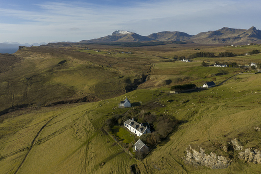 Aerial view of white cottages on green hills with grazing sheep and mountains in Isle of Skye Scotland.