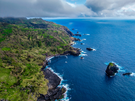 Aerial view of rugged cliffs meet the turbulent deep blue Atlantic where foamy white waves crash against the volcanic rock formations Faj&atilde; Grande Azores Portugal.
