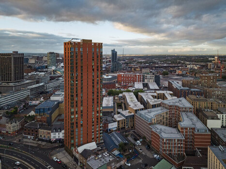 Aerial view of a tall red brick skyscraper rising above the urban landscape of Birmingham with surrounding rooftops and city buildings under a cloudy sky in Birmingham England United Kingdom.