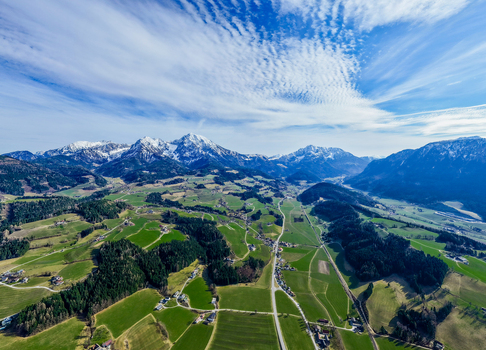 Aerial view of lush green fields contrasting with the snow capped mountains under a vibrant blue sky Windischgarsten Upper Austria Austria. Aerial view of lush green fields contrasting with the snow capped mountains under a vibrant blue sky Windischgarsten Upper Austria Austria.