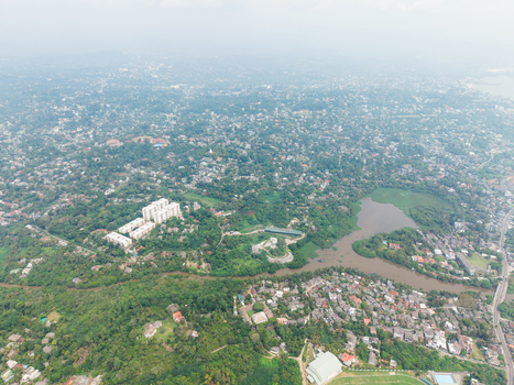 Aerial view of the urban landscape featuring dense green trees residential buildings and a winding waterway under a hazy sky in Galle Southern Province Sri Lanka. Aerial view of the urban landscape featuring dense green trees residential buildings and a winding waterway under a hazy sky in Galle Southern Province Sri Lanka.