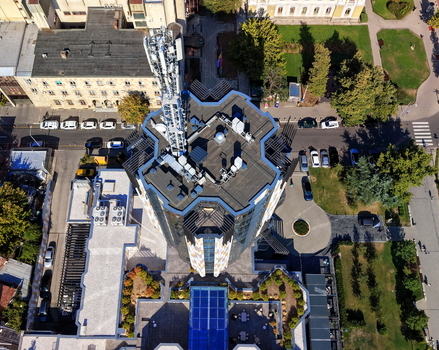Aerial view of a modern building with a prominent telecommunications tower on its roof surrounded by urban infrastructure parking areas and green spaces in Krusevac Rasina District Serbia. Aerial view of a modern building with a prominent telecommunications tower on its roof surrounded by urban infrastructure parking areas and green spaces in Krusevac Rasina District Serbia.