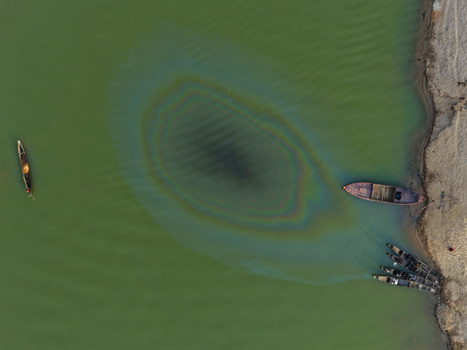 Aerial view of Jadukata River with traditional wooden boats moored along the sandy bank and an iridescent oil slick on the water surface in Sunamganj Sylhet Division Bangladesh. Aerial view of Jadukata River with traditional wooden boats moored along the sandy bank and an iridescent oil slick on the water surface in Sunamganj Sylhet Division Bangladesh.