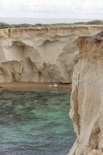 View of rugged limestone cliffs overlooking a small sandy cove and crystal clear turquoise water along the Mediterranean coast Syracuse Sicily Italy.
