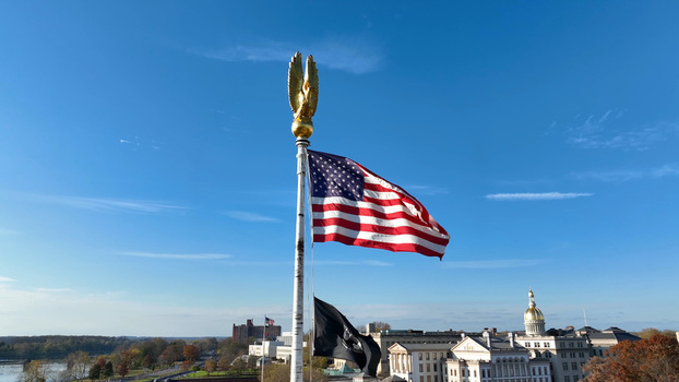 Aerial view of the American flag and POW MIA flag flying on a pole with the New Jersey State House dome in the background in Trenton New Jersey United States.