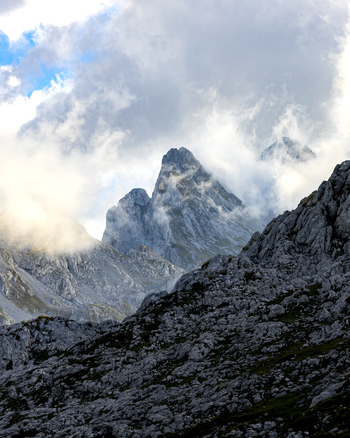 View of jagged peaks rise majestically amidst swirling clouds their rocky faces contrasting with the soft sky Picos de Europa Asturias Spain. View of jagged peaks rise majestically amidst swirling clouds their rocky faces contrasting with the soft sky Picos de Europa Asturias Spain.