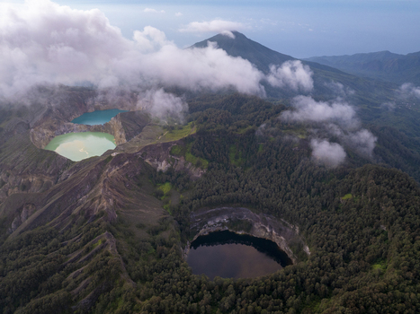 Aerial view of Kelimutu National Park featuring iconic tri colored volcanic crater lakes surrounded by lush forest and rugged mountain terrain in Detusoko East Nusa Tenggara Indonesia.