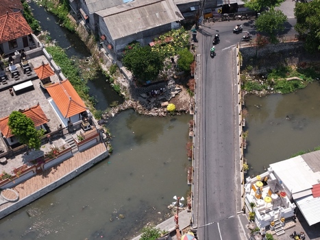 Aerial view of a bridge crossing a river in a residential area with traditional Balinese architecture lush trees and motorbikes in Kecamatan Denpasar Barat Bali Indonesia. Aerial view of a bridge crossing a river in a residential area with traditional Balinese architecture lush trees and motorbikes in Kecamatan Denpasar Barat Bali Indonesia.