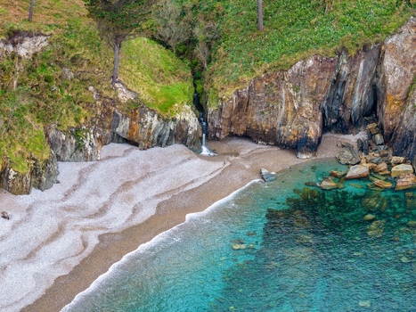 Aerial view of Silence Beach Viewpoint with its dramatic rocky cliffs a small waterfall and crystal clear turquoise water in Cudillero Asturias Spain.