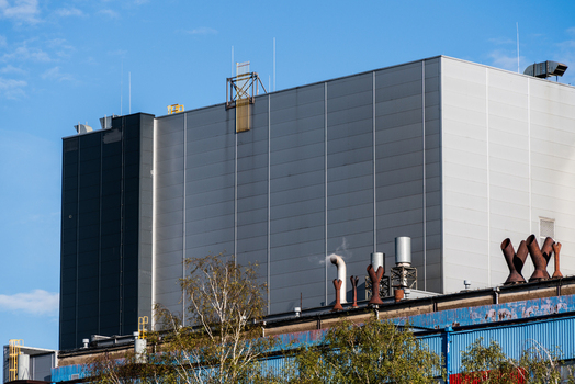 View of industrial building with metal siding and chimneys against a blue sky in Poland.