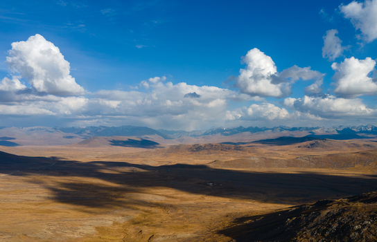 Aerial view of Deosai National Park with its vast golden plateau dramatic cloud formations and distant mountain range in Skardu Gilgit Pakistan.