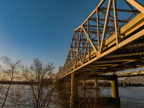 View of a massive steel truss bridge spanning the river during golden hour with bare trees in the foreground Louisville Kentucky United States. View of a massive steel truss bridge spanning the river during golden hour with bare trees in the foreground Louisville Kentucky United States.