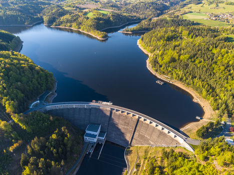 Aerial view of the Vir Dam a massive concrete structure holding back a large reservoir surrounded by dense green forests and rolling hills under a clear sky in Vir Kraj Vysocina Czechia. Aerial view of the Vir Dam a massive concrete structure holding back a large reservoir surrounded by dense green forests and rolling hills under a clear sky in Vir Kraj Vysocina Czechia.
