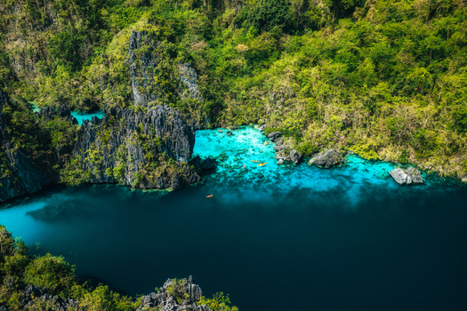 Aerial view of the turquoise waters of Big Lagoon surrounded by towering limestone cliffs and lush tropical vegetation in El Nido Bay Philippines. Aerial view of the turquoise waters of Big Lagoon surrounded by towering limestone cliffs and lush tropical vegetation in El Nido Bay Philippines.