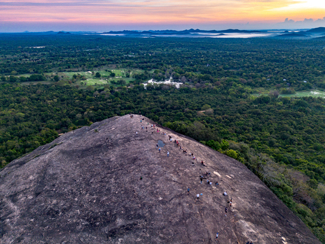 Aerial view of Pidurangala Rock with people hiking on the rocky summit surrounded by lush green jungle and misty horizon at sunset in Sigiriya Central Province Sri Lanka. Aerial view of Pidurangala Rock with people hiking on the rocky summit surrounded by lush green jungle and misty horizon at sunset in Sigiriya Central Province Sri Lanka.
