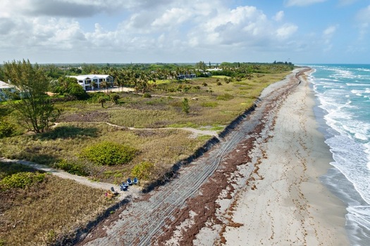 Aerial view of the sun kissed beach where the turquoise ocean meets the sandy shore with glimpses of lush vegetation and houses Jupiter Island Florida United States. Aerial view of the sun kissed beach where the turquoise ocean meets the sandy shore with glimpses of lush vegetation and houses Jupiter Island Florida United States.