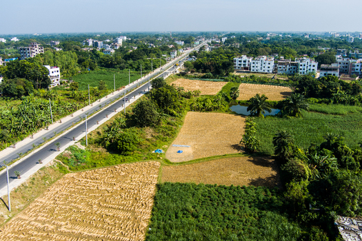 Aerial view of agricultural fields a paved road and residential buildings in the outskirts of Rajshahi Rajshahi Division Bangladesh.