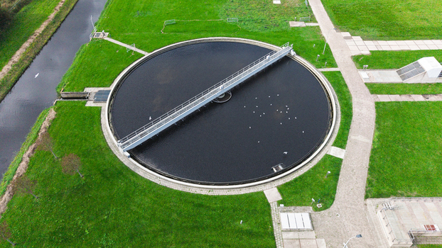 Aerial view of a circular wastewater treatment plant with a central bridge and dark water surrounded by green grass and a canal in Warmenhuizen North Holland Netherlands. Aerial view of a circular wastewater treatment plant with a central bridge and dark water surrounded by green grass and a canal in Warmenhuizen North Holland Netherlands.