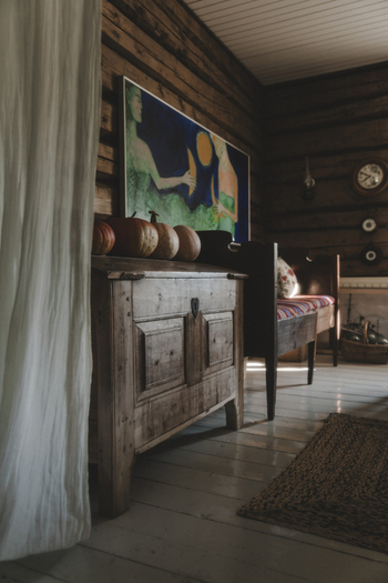 Laane County Estonia 04 October 2024 View of a rustic interior on Vormsi island featuring a wooden chest topped with pumpkins a colorful painting on log walls and a cozy bench.