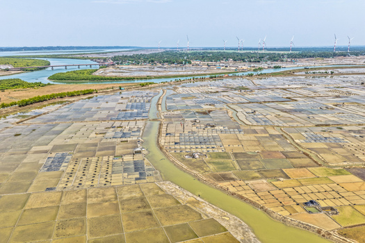 Aerial view of patchwork fields reflecting the sky s muted tones divided by winding waterways leading to a distant bridge Cox s Bazar Chittagong Division Bangladesh. Aerial view of patchwork fields reflecting the sky s muted tones divided by winding waterways leading to a distant bridge Cox s Bazar Chittagong Division Bangladesh.