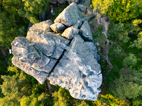 Aerial view of Popova Skala rock formation with a metal walkway surrounded by lush forest in the golden hour light in Hradek nad Nisou Liberec Region Czechia. Aerial view of Popova Skala rock formation with a metal walkway surrounded by lush forest in the golden hour light in Hradek nad Nisou Liberec Region Czechia.