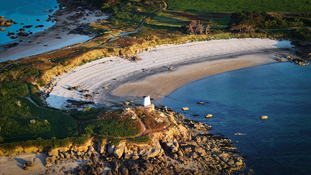 Aerial view of a serene cove with a white building nestled amongst rocky outcrops and golden sands meeting the turquoise sea Carantec Brittany France. Aerial view of a serene cove with a white building nestled amongst rocky outcrops and golden sands meeting the turquoise sea Carantec Brittany France.