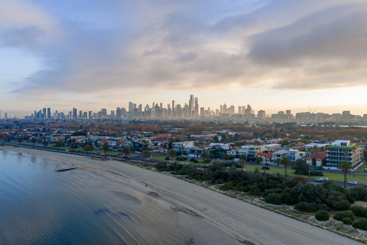 Aerial view of the Melbourne skyline rising above St Kilda West beach with Beaconsfield Parade and car traffic in Melbourne Victoria Australia. Aerial view of the Melbourne skyline rising above St Kilda West beach with Beaconsfield Parade and car traffic in Melbourne Victoria Australia.