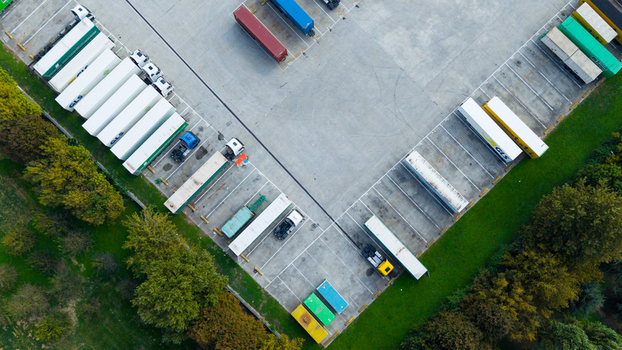 Aerial view of commercial trailers and shipping containers parked in an organized logistics facility surrounded by lush trees in Milan Lombardy Italy.
