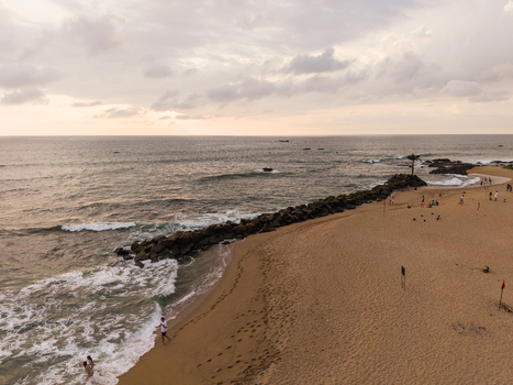 Aerial view of people walking on a sandy beach next to a stone breakwater with waves crashing under a cloudy sky in Galle Southern Province Sri Lanka.