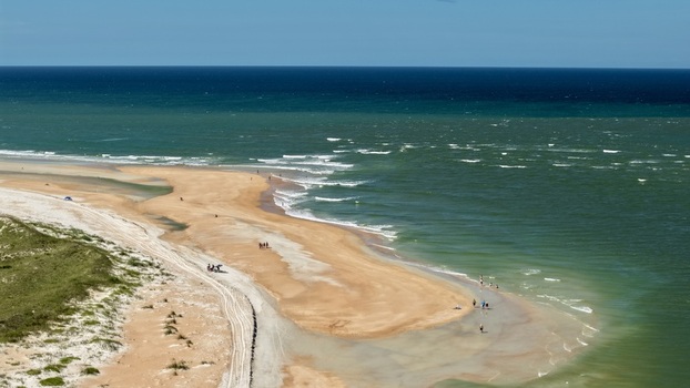 Aerial view of Matanzas Inlet featuring sandy beach turquoise ocean and dunes under clear sky with people walking along the shore in St. Johns County Florida United States. Aerial view of Matanzas Inlet featuring sandy beach turquoise ocean and dunes under clear sky with people walking along the shore in St. Johns County Florida United States.