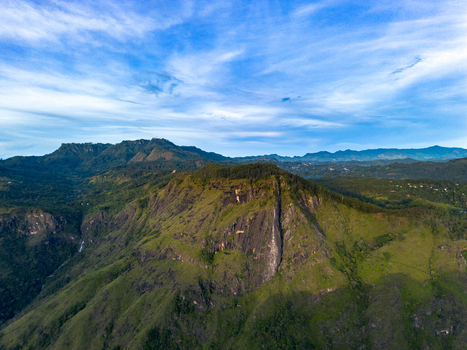 Aerial view of Little Adam s Peak featuring lush green mountain slopes under a bright blue sky with scattered clouds in Badulla Uva Province Sri Lanka. Aerial view of Little Adam s Peak featuring lush green mountain slopes under a bright blue sky with scattered clouds in Badulla Uva Province Sri Lanka.