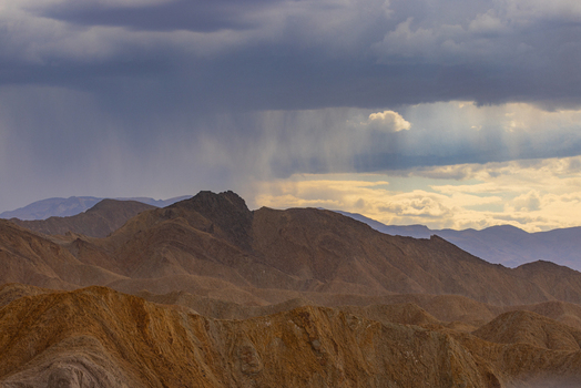 View of the rugged desert mountains of Death Valley National Park under a dramatic stormy sky with rain showers falling in the distance United States.