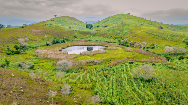 Aerial view of a small crater lake nestled between rolling green hills and agricultural fields in Mangu Plateau Nigeria. Aerial view of a small crater lake nestled between rolling green hills and agricultural fields in Mangu Plateau Nigeria.