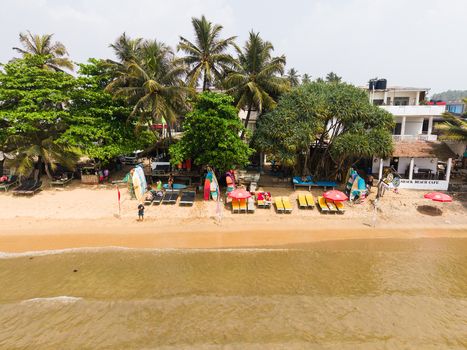 Aerial view of Dewata Beach Road featuring surfboards sun loungers and palm trees along the sandy shore in Galle Southern Province Sri Lanka.