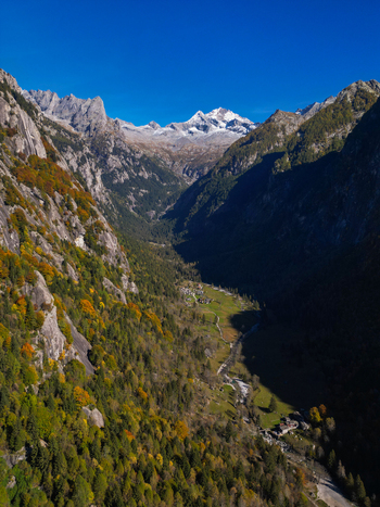 Aerial view of Val di Mello valley with autumn foliage on steep granite cliffs and snow capped peaks under a clear blue sky Val Masino Lombardia Italy. Aerial view of Val di Mello valley with autumn foliage on steep granite cliffs and snow capped peaks under a clear blue sky Val Masino Lombardia Italy.