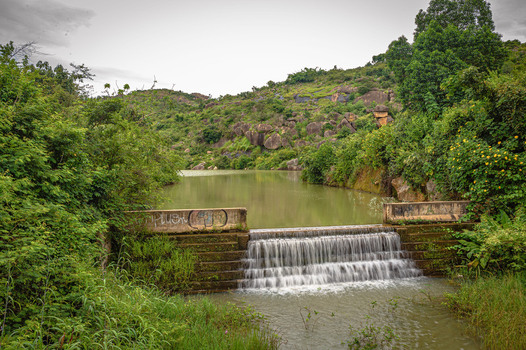 View of Lamingo Dam with a small waterfall flowing into a reservoir surrounded by lush green hills and rocky terrain in Jos Plateau Nigeria.