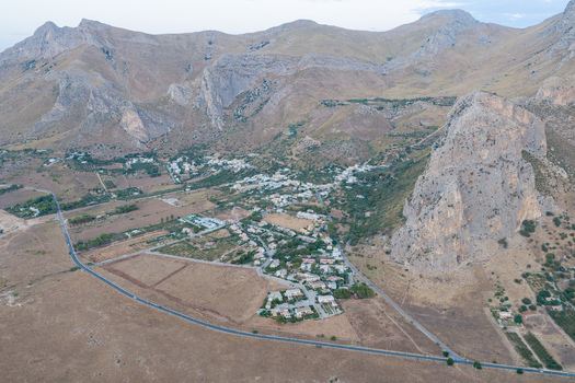 Aerial view of Riserva Naturale Orientata dello Zingaro featuring rugged limestone cliffs dry landscape and scattered buildings near the road in San Vito Lo Capo Sicilia Italy. Aerial view of Riserva Naturale Orientata dello Zingaro featuring rugged limestone cliffs dry landscape and scattered buildings near the road in San Vito Lo Capo Sicilia Italy.