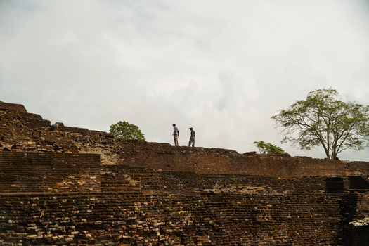 View of the ancient stone ruins of Sigiriya fortress with two people standing on the historic walls under a cloudy sky Sigiriya Central Province Sri Lanka. View of the ancient stone ruins of Sigiriya fortress with two people standing on the historic walls under a cloudy sky Sigiriya Central Province Sri Lanka.