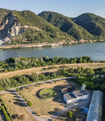 Aerial view of circular clarifier tanks at a wastewater treatment plant situated near the Rhone river and lush green hills in Le Pouzin Auvergne Rhone Alpes France.