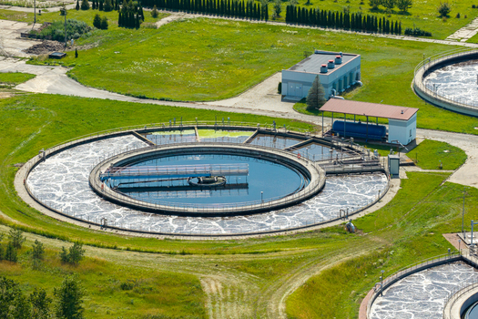 Aerial view of a wastewater treatment plant with circular sedimentation tanks and aeration basins surrounded by green grass in Poland.