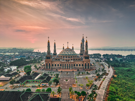 Aerial view of Baitul Muttaqien Mosque at the East Kalimantan Islamic Center with its large dome and minarets under a sunset sky in Samarinda East Kalimantan Indonesia.