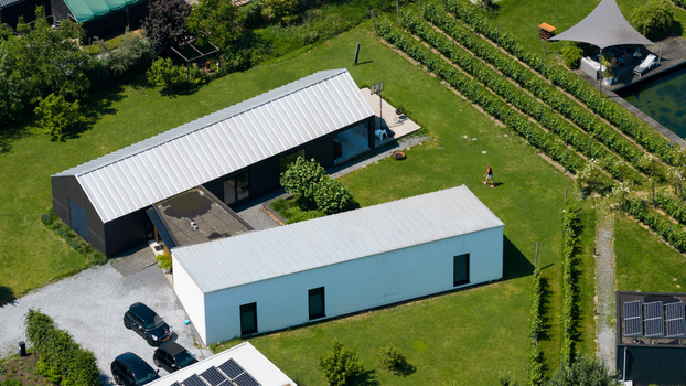 Aerial view of Ecodorp Bolderburen featuring a modern house with white and dark sections surrounded by a lush green lawn solar panels and garden rows in Almere Flevoland Netherlands. Aerial view of Ecodorp Bolderburen featuring a modern house with white and dark sections surrounded by a lush green lawn solar panels and garden rows in Almere Flevoland Netherlands.