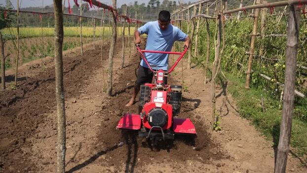 View of a man operating a red power tiller in a farm field Nepal. View of a man operating a red power tiller in a farm field Nepal.