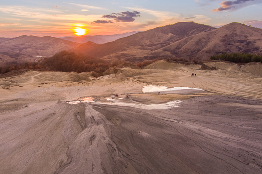 Aerial view of the Mud Volcanoes of Paclele Mari featuring unique grey mud formations barren landscape and distant mountains under a golden sunset sky in Paclele Buzau County Romania.