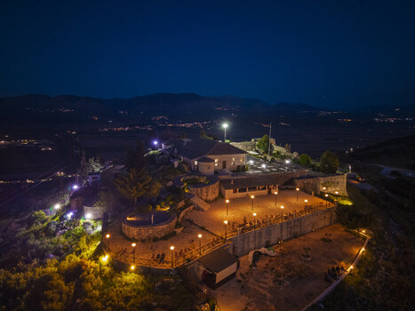 Aerial view of Lekuresi Castle illuminated at night featuring historic stone walls a courtyard with warm lighting and surrounding hills in Saranda Vlore County Albania. Aerial view of Lekuresi Castle illuminated at night featuring historic stone walls a courtyard with warm lighting and surrounding hills in Saranda Vlore County Albania.